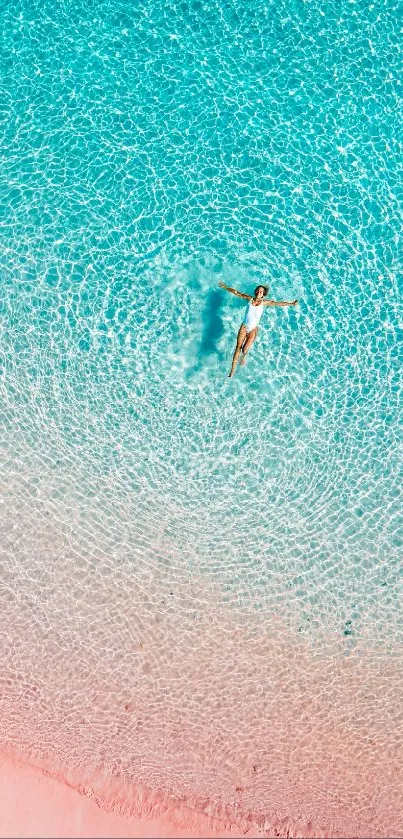 Top down view of a person in turquoise ocean near a pink-sand beach.