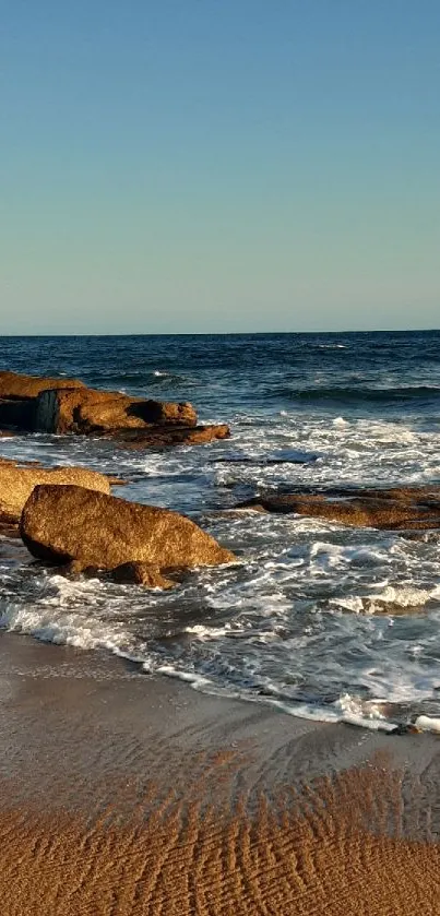 Beach scene with rocks and waves at sunset.