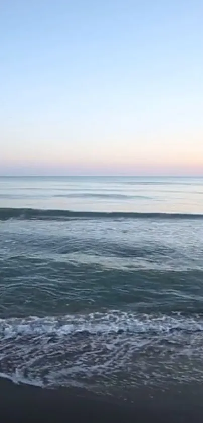 Serene beach at sunset with ocean waves and pastel sky.