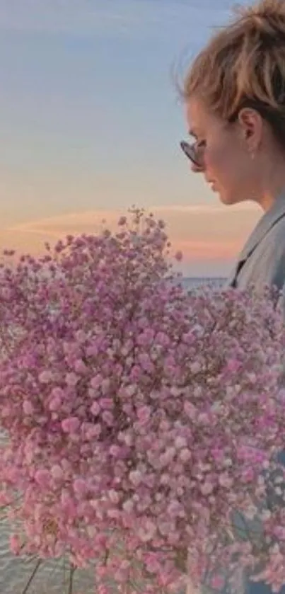 Woman with pink flowers by beach at sunset.