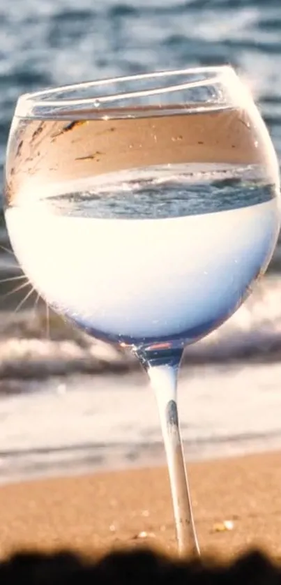 Glass of water reflecting ocean on a beach scene.