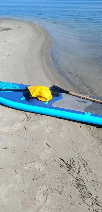 A blue paddleboard and sand at the beach with a clear ocean view.