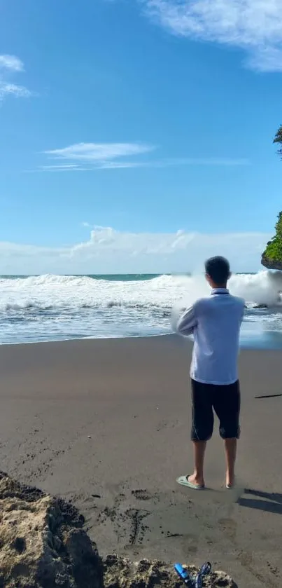 A person standing on a peaceful beach with a bright blue sky and calm ocean waves.