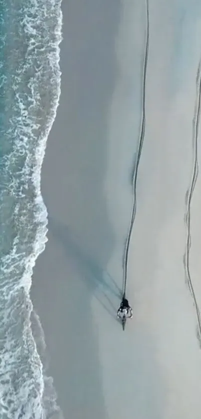 Aerial view of a motorcycle riding along a sandy beach by the ocean.