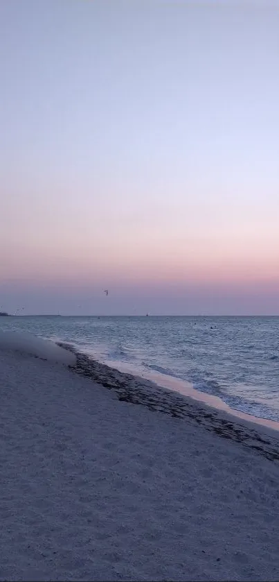 Serene sunset over a beach with pastel sky and gently sweeping waves.