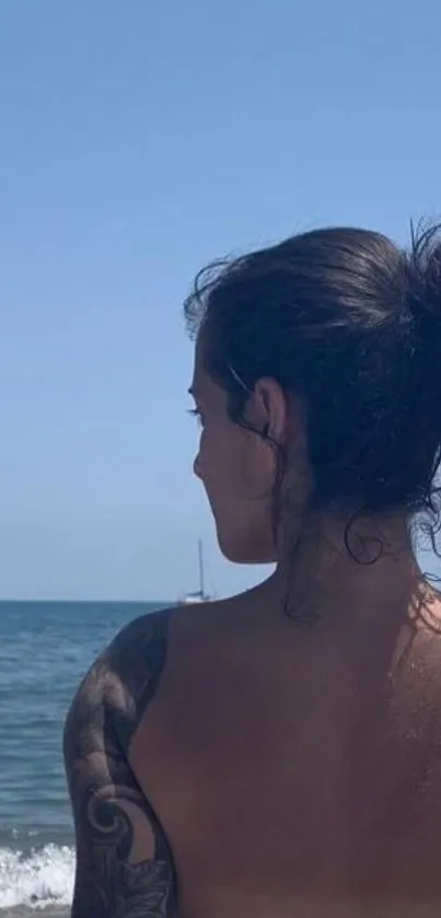 Tattooed person gazing at peaceful ocean beach.