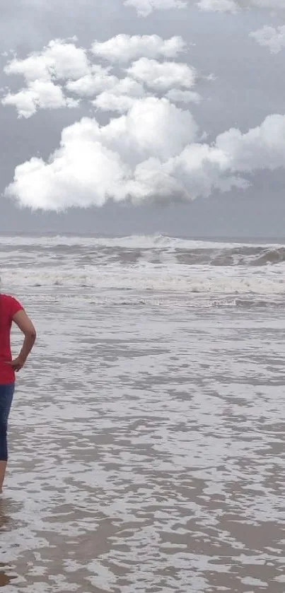 Woman stands on a calm beach with stormy skies.