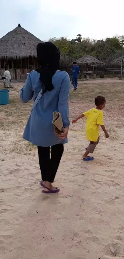 A woman and child walking on a sandy beach with huts in the background.