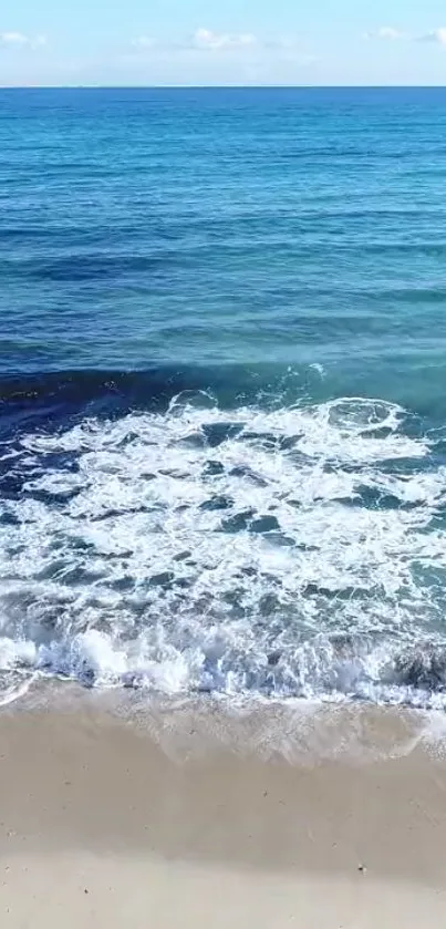 A serene beach view with waves crashing on the sandy shore under a blue sky.