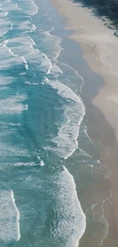 Aerial view of waves crashing on a serene sandy beach under a clear sky.