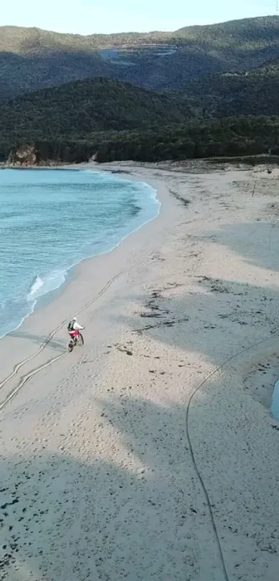 Two riders on a deserted beach with mountains in the background.