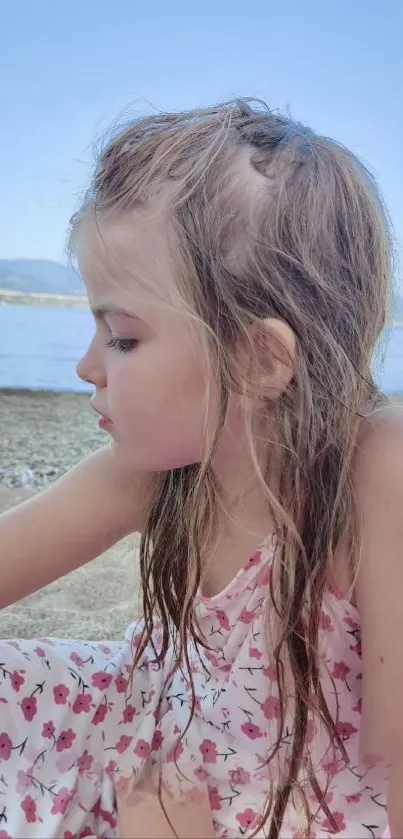 A young girl in a floral dress at a peaceful beach, gazing at the horizon.