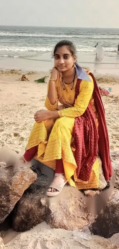 Woman in yellow dress sitting on beach rocks with ocean view.