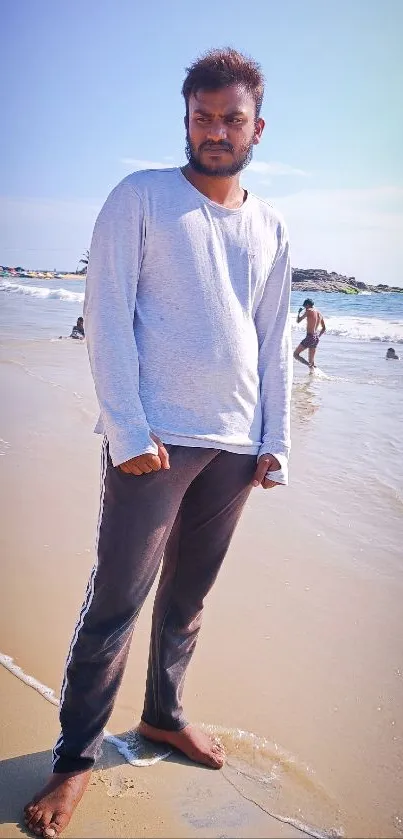 A man standing on a sandy beach under a clear blue sky.