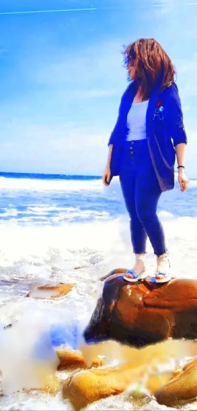 Woman stands on rock by ocean under a clear blue sky.