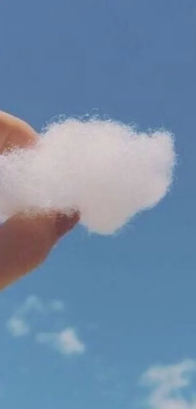 Hand holding cloud against a blue sky.