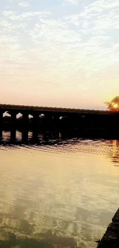 Sunset over a river with a silhouetted bridge and pastel sky reflections.