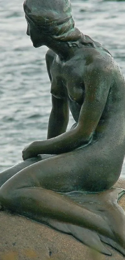 Bronze mermaid statue on rock by the water.