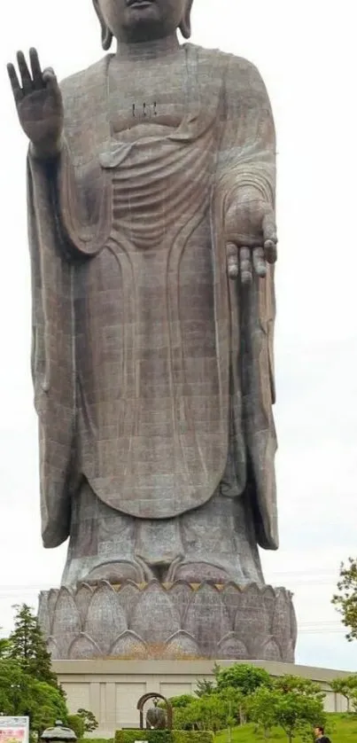 Tall Buddha statue with colorful flowers at base in outdoor setting.