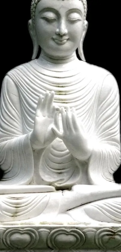 White Buddha sculpture in serene meditation pose on black background.