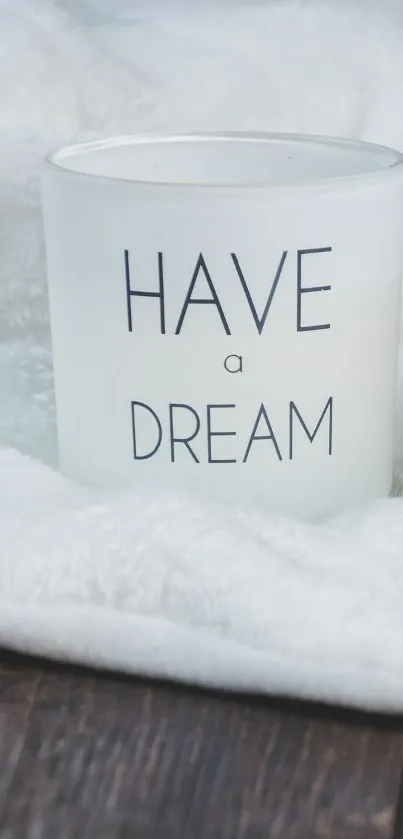 White candle with 'Have a Dream' text on a soft, white blanket.