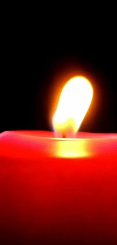 Close-up of a red candle with a glowing flame against a black background.