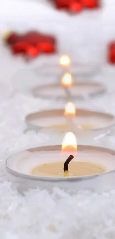 Lit candles on a snowy surface with red decorations in the background.