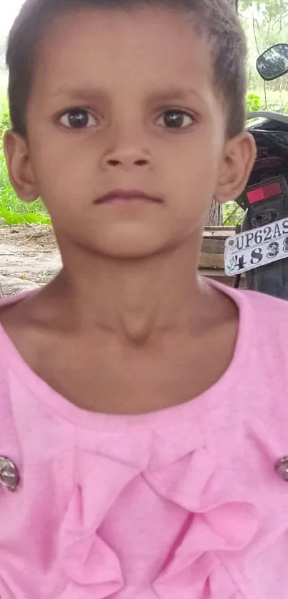 Child in pink shirt with serene outdoor background.