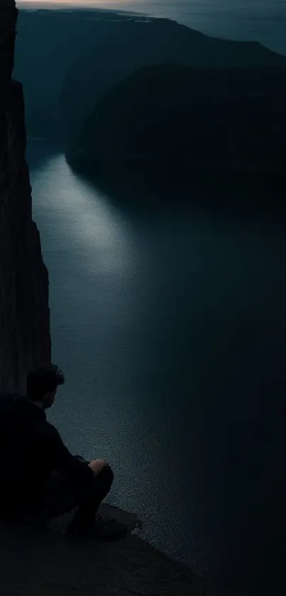 Man sitting on cliff, evening sky and water.