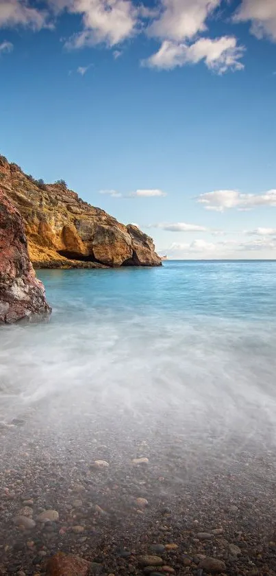 Serene beach with blue sky and rocky shore, perfect mobile wallpaper.