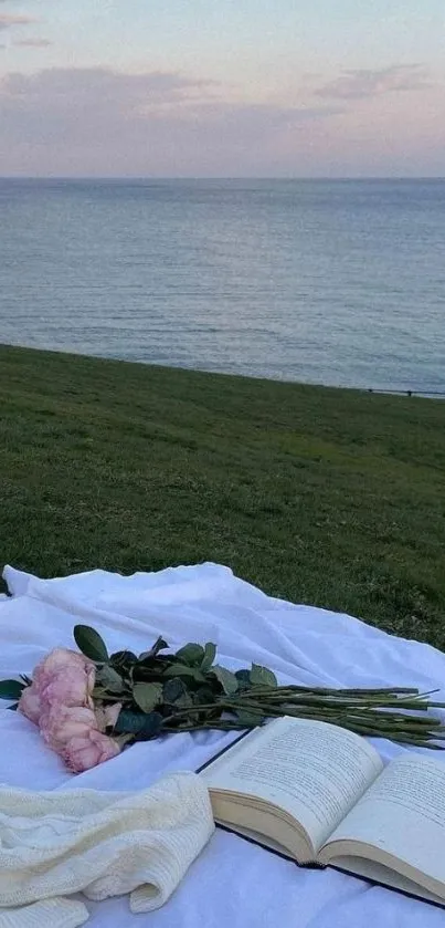 Serene coastal picnic setup with ocean view, book, and pink flowers.