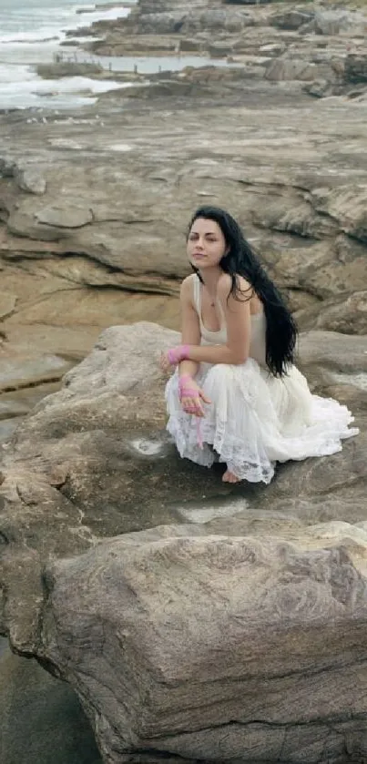 Woman in white dress sitting on coastal rocks.