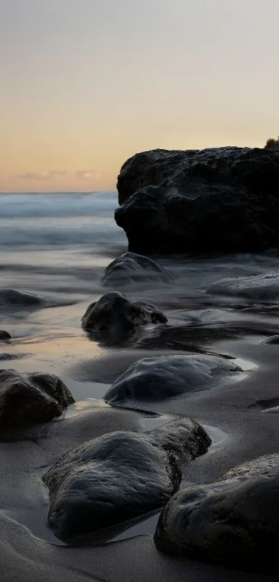 Serene coastal sunset with black rocks and calming waves.