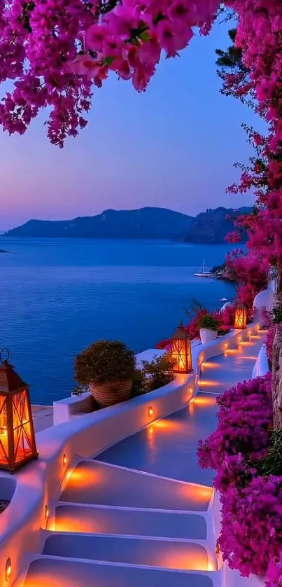 Lantern-lit path with pink flowers by the sea at sunset.