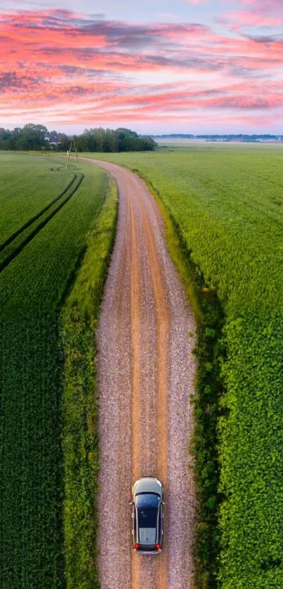 Aerial view of a car on a countryside road at sunset with green fields.