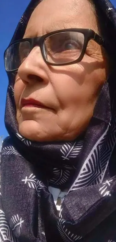 Elderly woman in glasses and scarf under a blue sky.