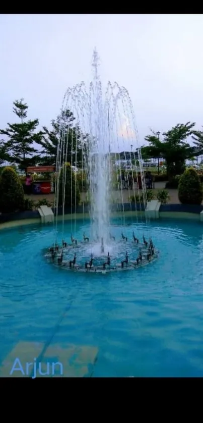 A serene park fountain with blue water and surrounding greenery.