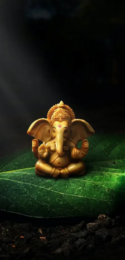 Golden Ganesha statue resting on a green leaf against a dark background.