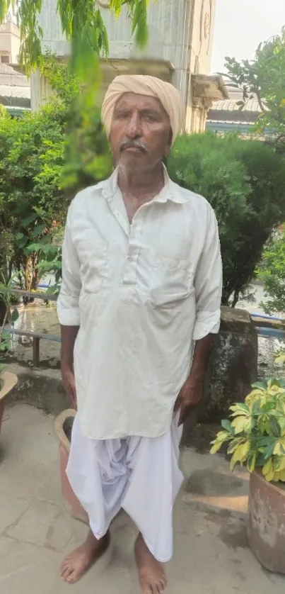 Man in traditional attire stands in lush garden.