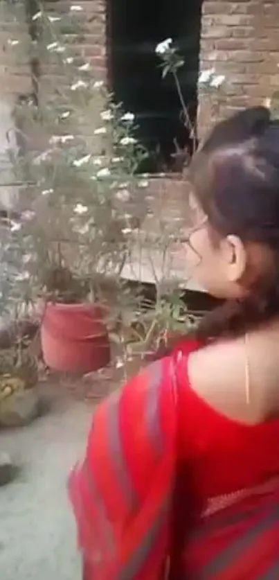 Woman in red saree admires garden flowers.