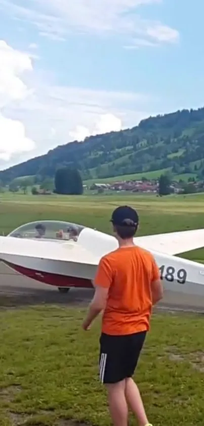 Glider plane at rest in lush green mountain landscape under a blue sky.