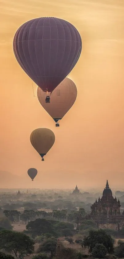 Four hot air balloons float over a scenic, ancient landscape at sunset.