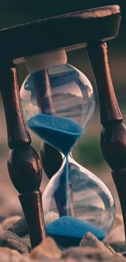 Hourglass with blue sand placed on pebbles.