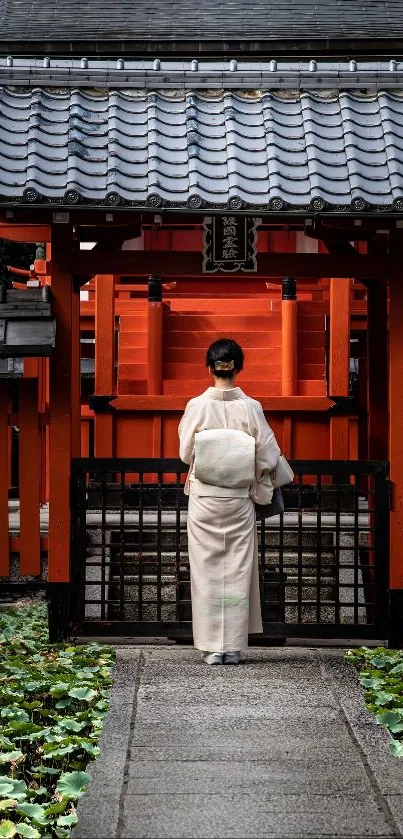 Person in kimono stands before a red Japanese temple gate, surrounded by greenery.