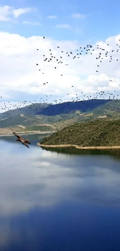 A serene lake with a bird flock flying over mountains and clear blue sky.