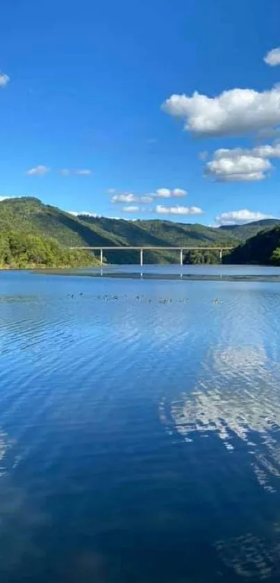 Beautiful lake with bridge and hills under a clear blue sky.