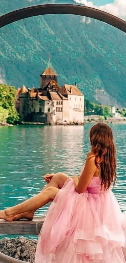 Woman in pink dress overlooking a lake castle with mountains in background.