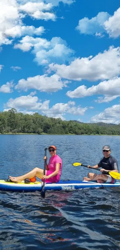 Two people kayaking on a serene lake under a blue sky.