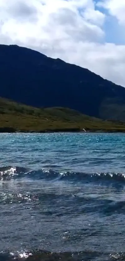 Serene mountain lake under blue sky with hills in the background.