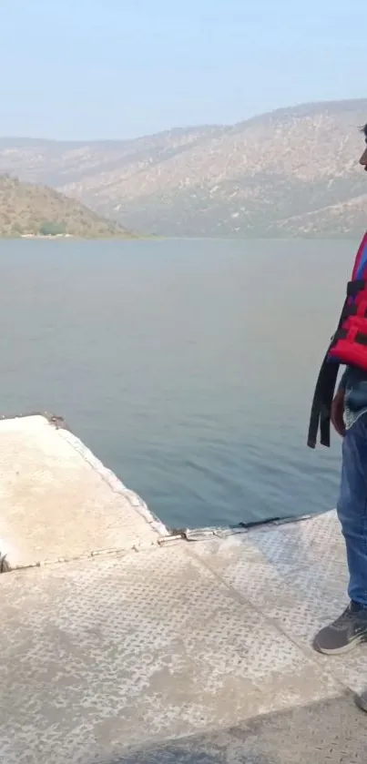 Person in life jacket by a serene lakeside with mountainous backdrop.